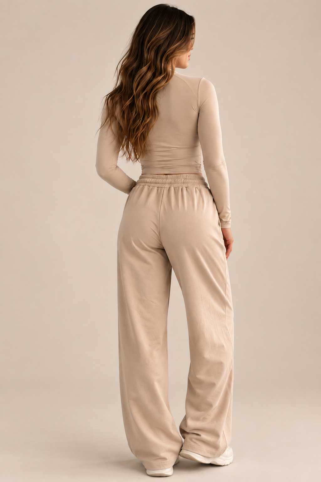 A woman shown from the back wearing a beige ribbed long-sleeve top and matching wide-leg sweatpants against a plain beige studio background.