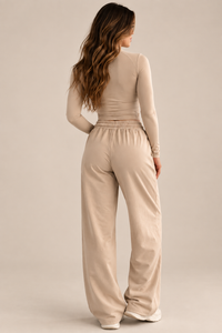 A woman shown from the back wearing a beige ribbed long-sleeve top and matching wide-leg sweatpants against a plain beige studio background.