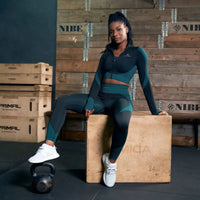 Woman in athletic wear sitting on a wooden box with gym equipment in the background