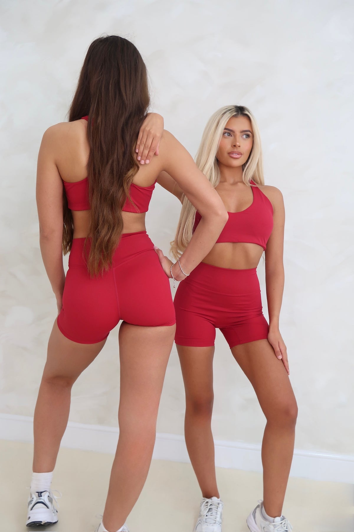 Two women in red athletic outfits standing back-to-back against a white wall.