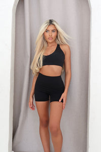 Woman wearing a black sports bra and shorts against a neutral background
