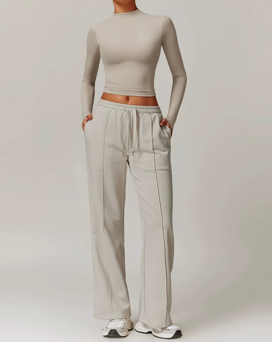 Person wearing a beige long-sleeve crop top and light gray sweatpants on a plain background