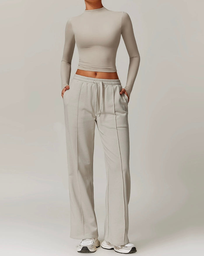 Person wearing a beige long-sleeve crop top and light gray sweatpants on a plain background
