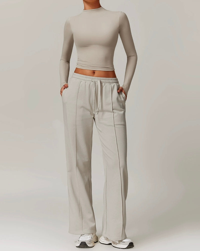 Person wearing a beige long-sleeve crop top and light gray sweatpants on a plain background