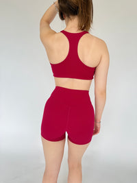 Person wearing a red sports bra and shorts on a plain background
