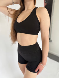 Person wearing a black sports bra and shorts set on a neutral background
