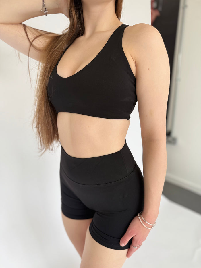 Person wearing a black sports bra and shorts set on a neutral background