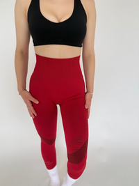 Person wearing a black sports bra and red leggings on a white background