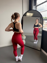 Woman in red leggings and black sports bra standing in front of a mirror.