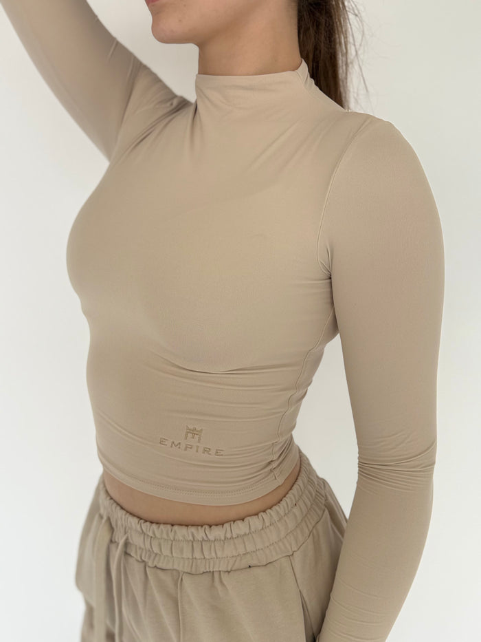Person wearing a beige long-sleeve top with 'EMPIRE' branding on a plain background
