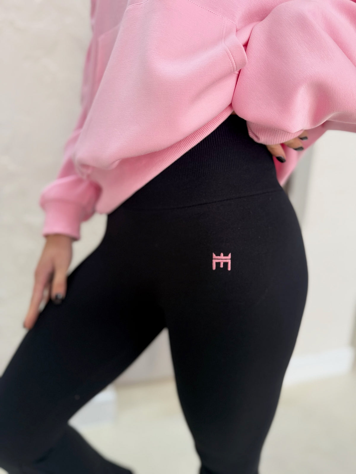 Person wearing black leggings with a pink logo and a pink sweatshirt on a light background